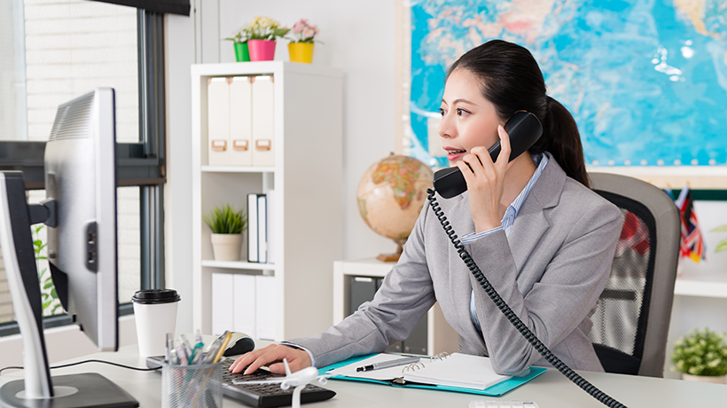 Travel agent working in travel agency on the phone to customer