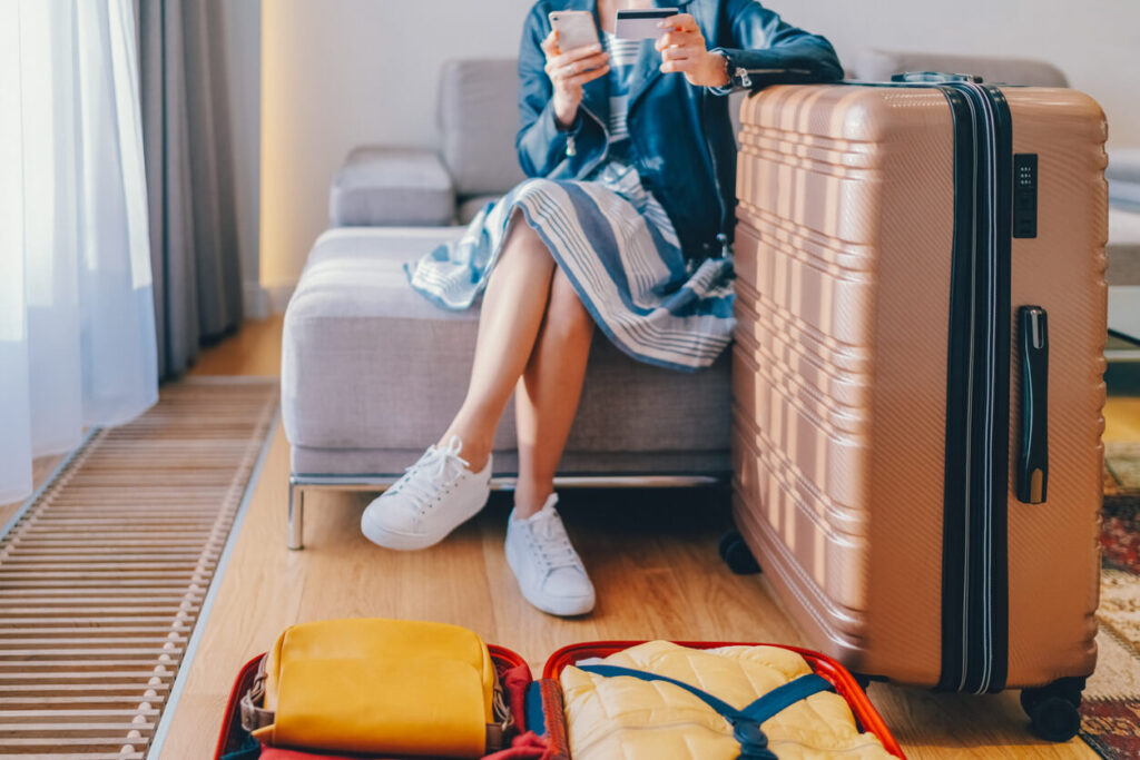 here is an image of a woman sitting with a suitcase booking a trip online
