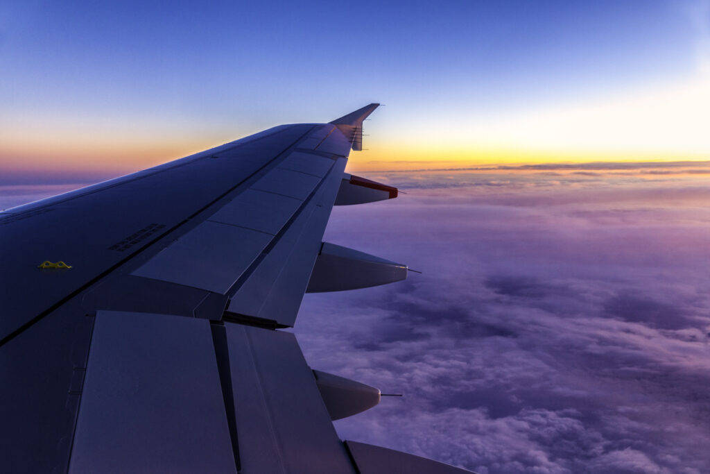 View of airplane wing above the clouds at sunrise, symbolising premium flight deals with a business class travel consolidator